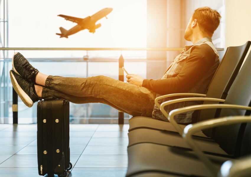 man sitting on gang chair with feet on luggage looking at airplane. Punta Cana Vacation Package